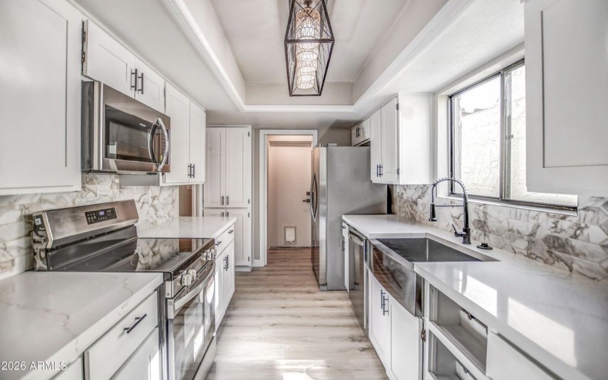The finished galley kitchen after the Casa Grande rehab — white shaker cabinets, quartz counters, marble-look backsplash, stainless appliances and a farmhouse sink